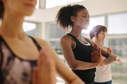 three women meditating in a class with eyes closed and hands folded